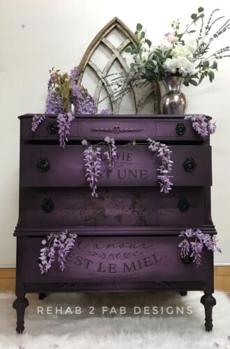 plum dresser with white wall and wooden frame on top of dresser. Grapes accent the color of this piece